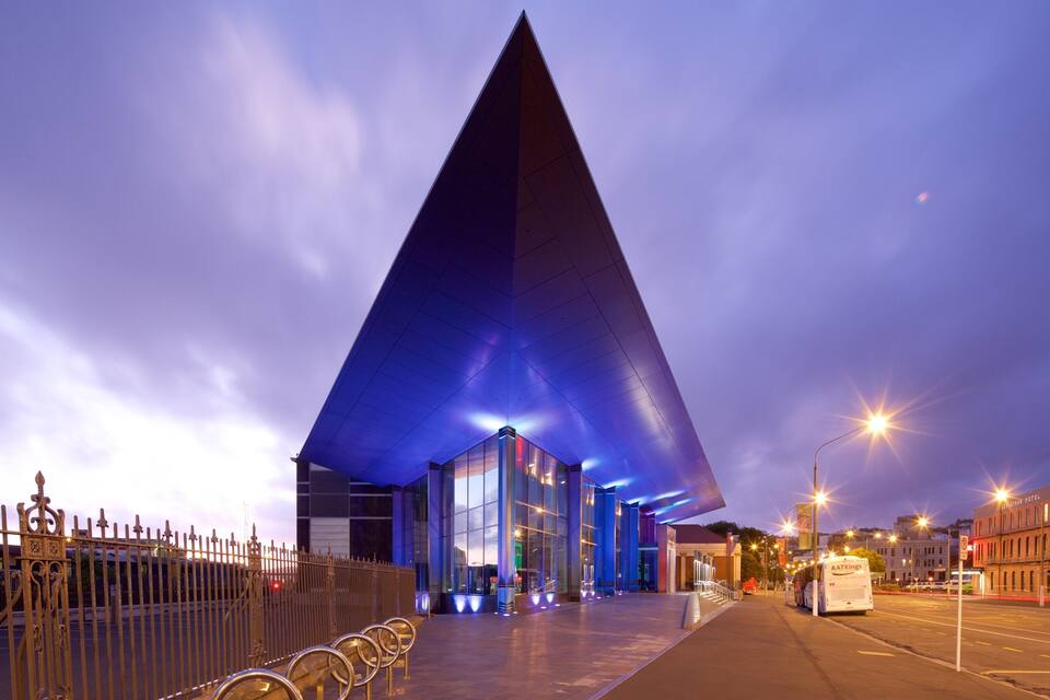 A modern building with a large triangular roof and glass windows, surrounded by a metal fence and street lamps.
