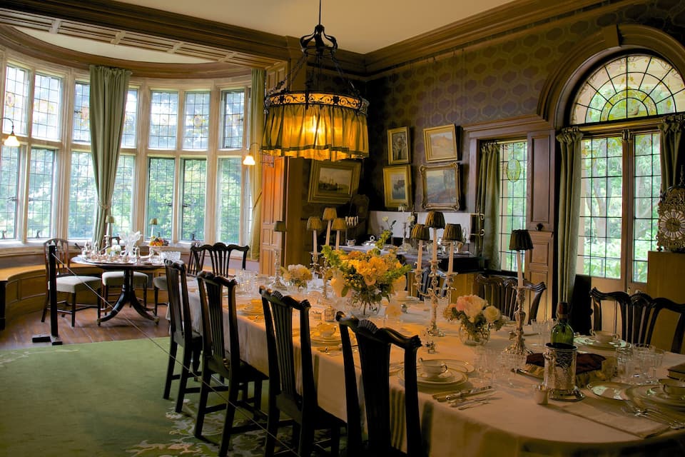A formal dining room with a long table set for a meal, surrounded by chairs.