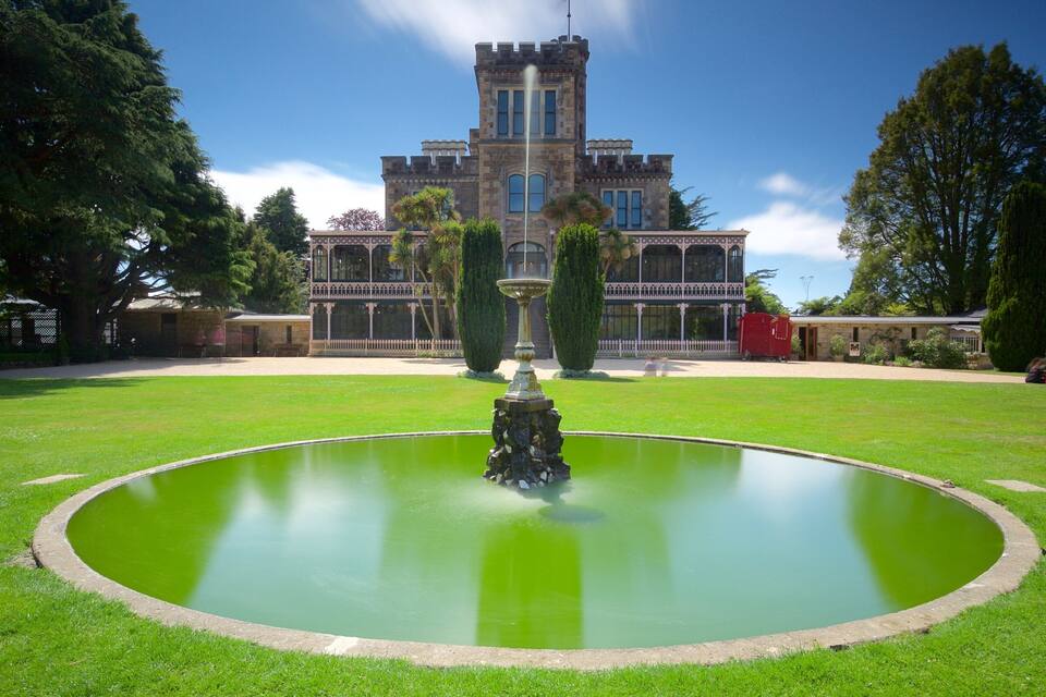 A large building with a tower, a fountain in the middle of a circular lawn, and trees around.