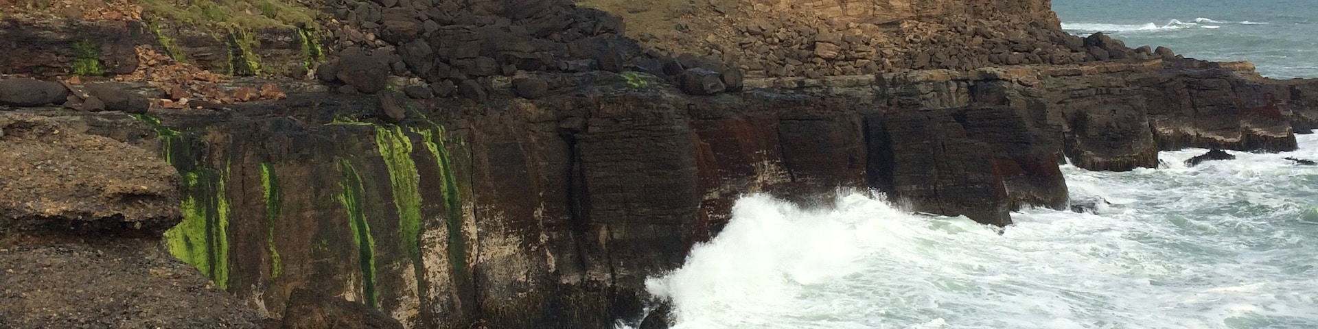 A rocky coastline with waves crashing against the shore and a lighthouse on a cliff.