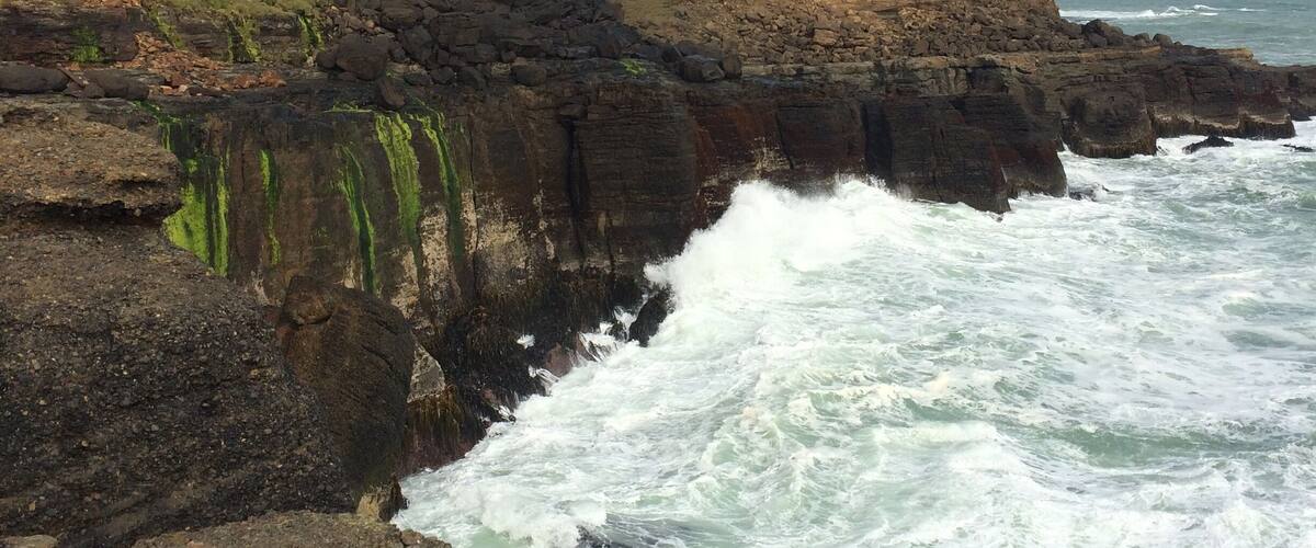 A rocky coastline with waves crashing against the shore and a lighthouse on a cliff.