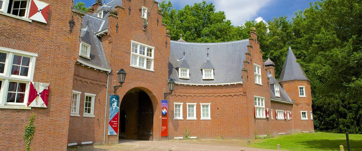 A historic brick building with a large arched entrance, multiple windows, and a flagpole with flags.