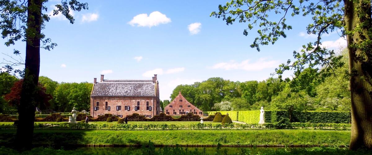 A large brick building surrounded by lush greenery and a pond.