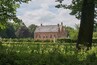 A historic brick building with a sloped roof and chimneys, surrounded by lush greenery and a well-maintained garden.