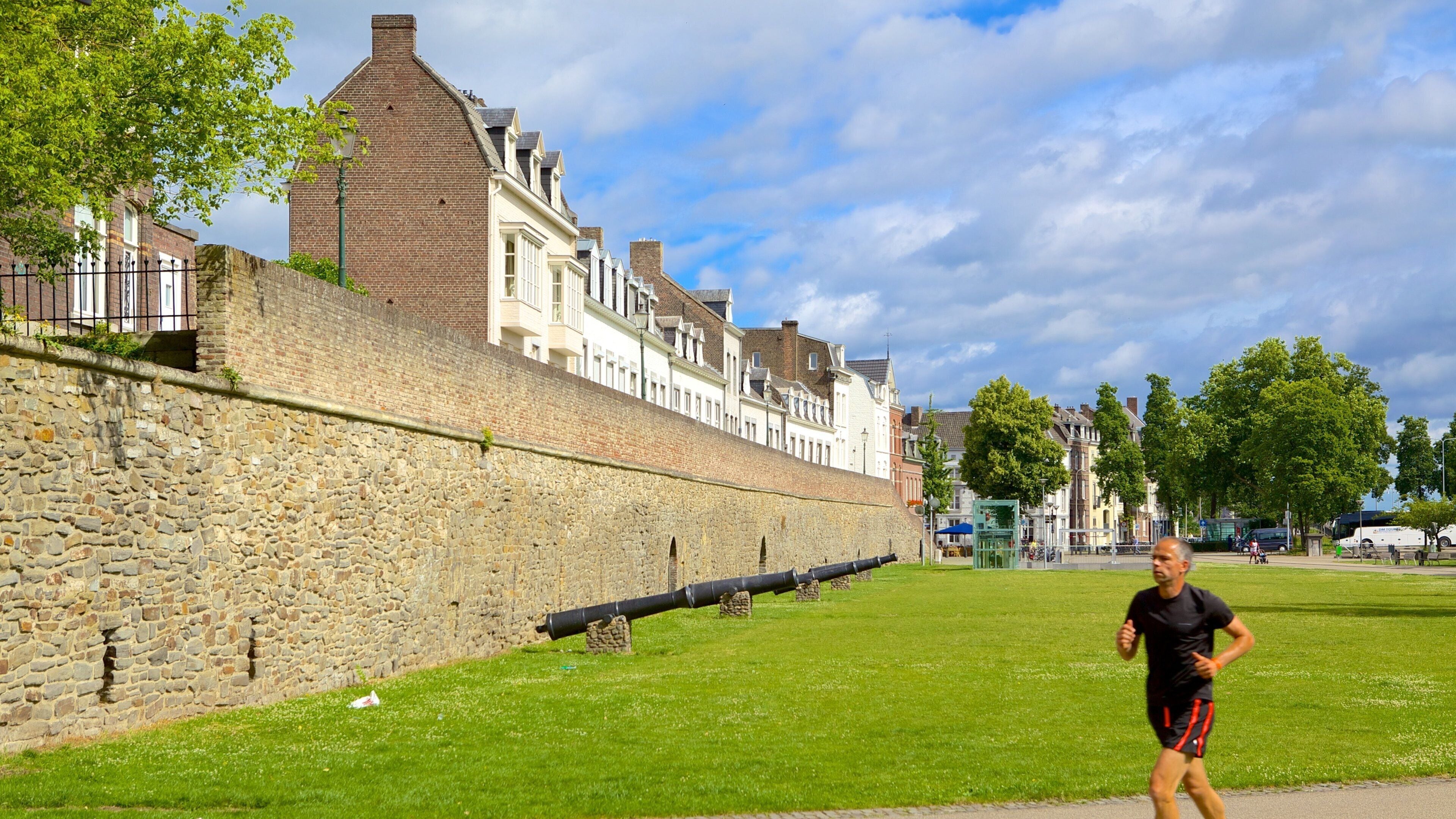A historic stone wall with a cannon, a running track, and traditional European buildings in the background.