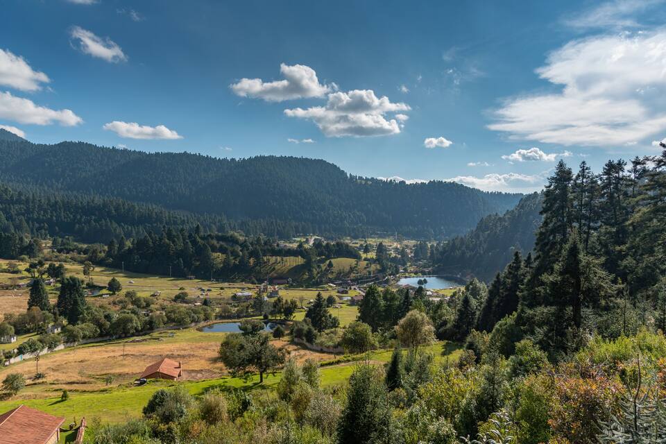 A valley with a lake, surrounded by forested hills and scattered houses.