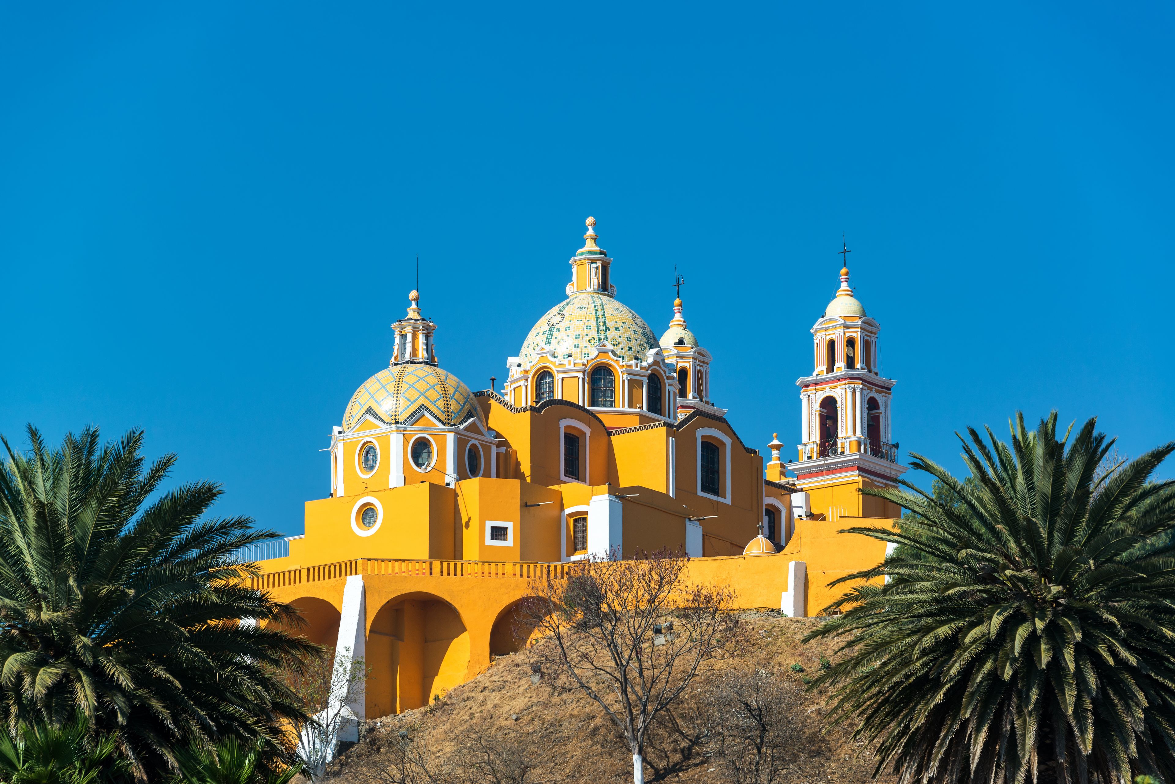 A yellow church with multiple domes and bell towers against a clear blue sky.
