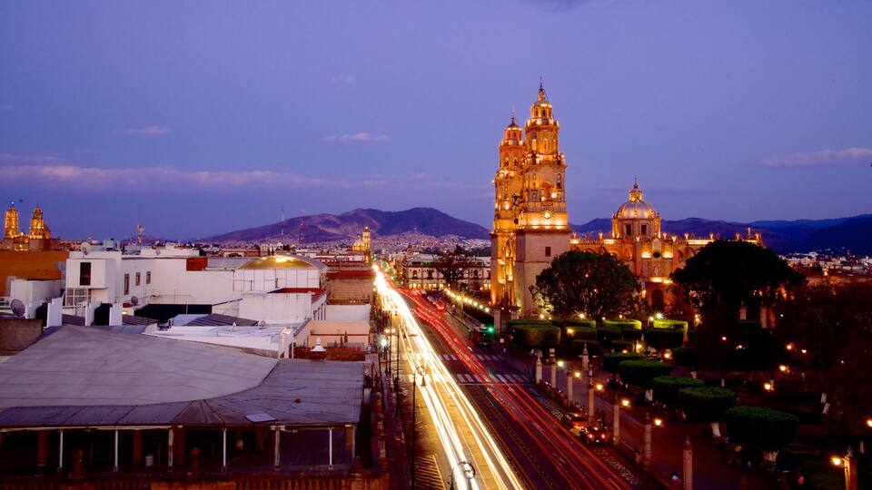 A cityscape at dusk with illuminated buildings and a prominent tower.
