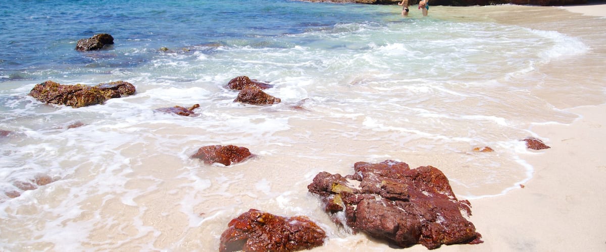 Ein Strand mit klarem Wasser, Felsen und einer steilen Klippe.