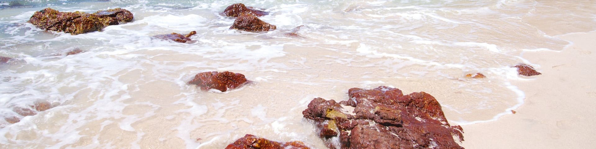 A beach with clear water, rocks, and a rocky cliff.