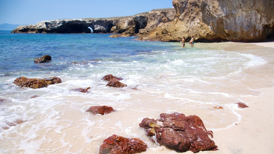 Ein Strand mit klarem Wasser, Felsen und einer steilen Klippe.