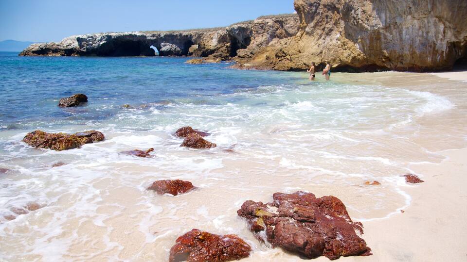 A beach with clear water, rocks, and a rocky cliff.