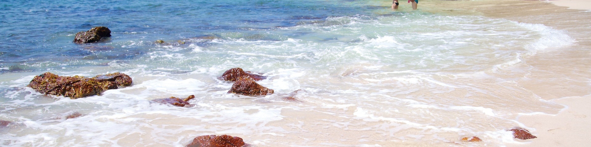 Una playa con agua cristalina, rocas y un acantilado rocoso.