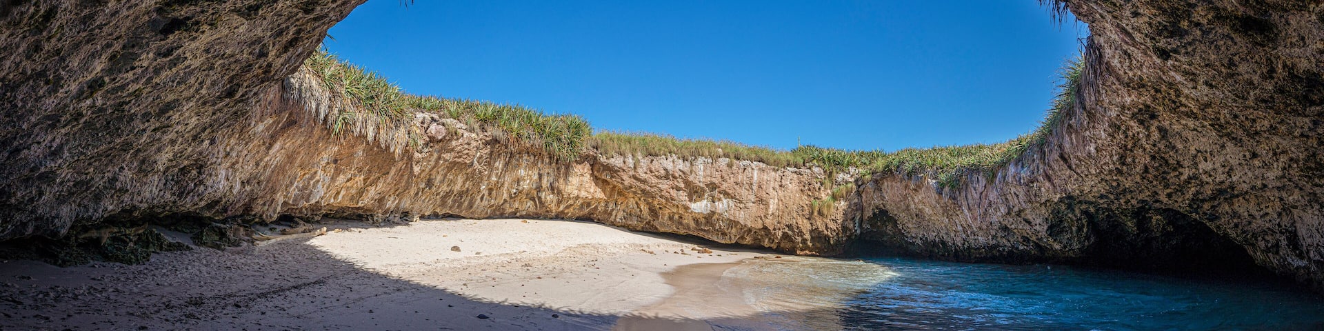 A natural cave opening to a beach with clear blue water and sandy shore.