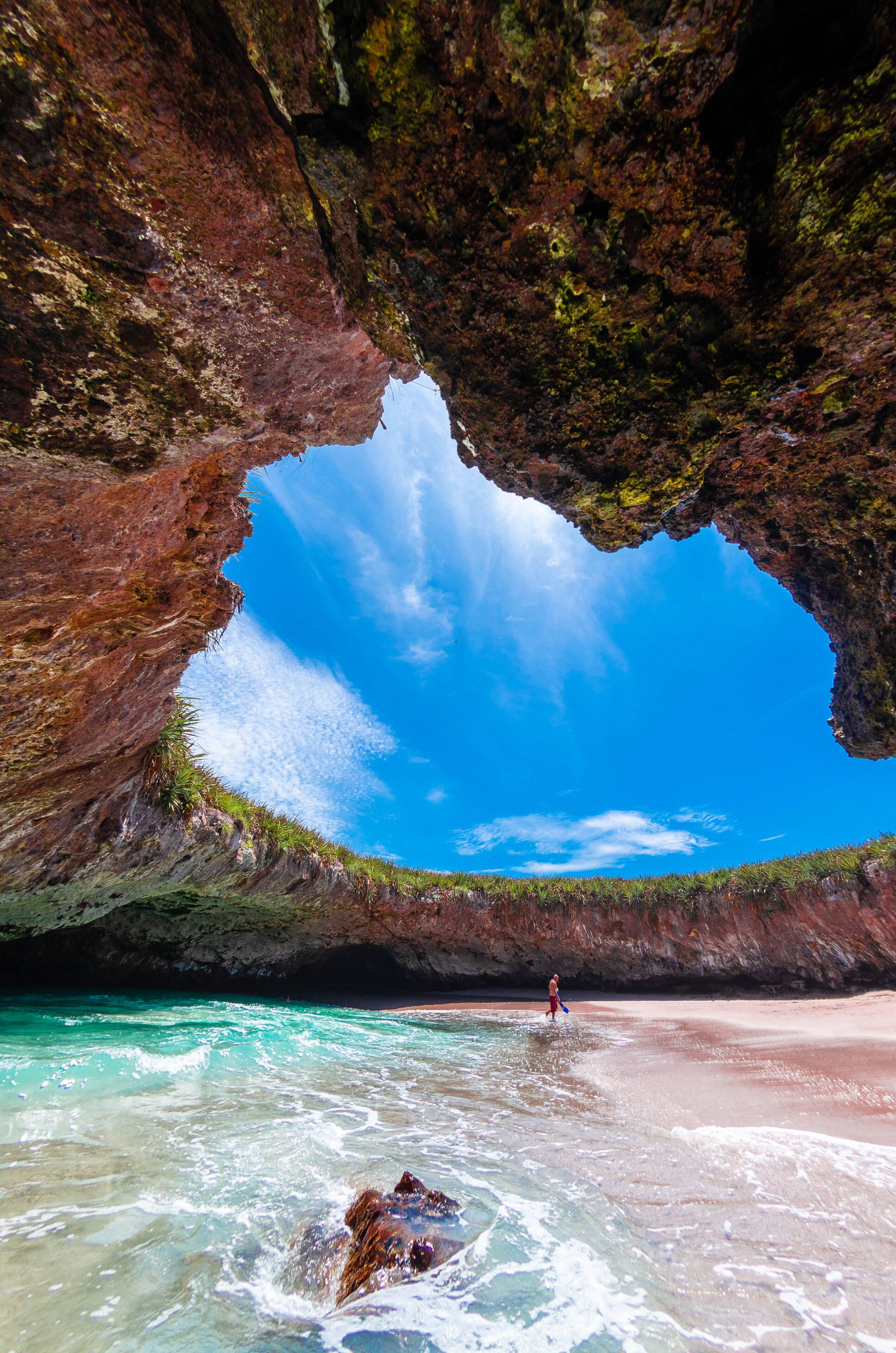 A natural rock formation with a clear blue sky above a beach.