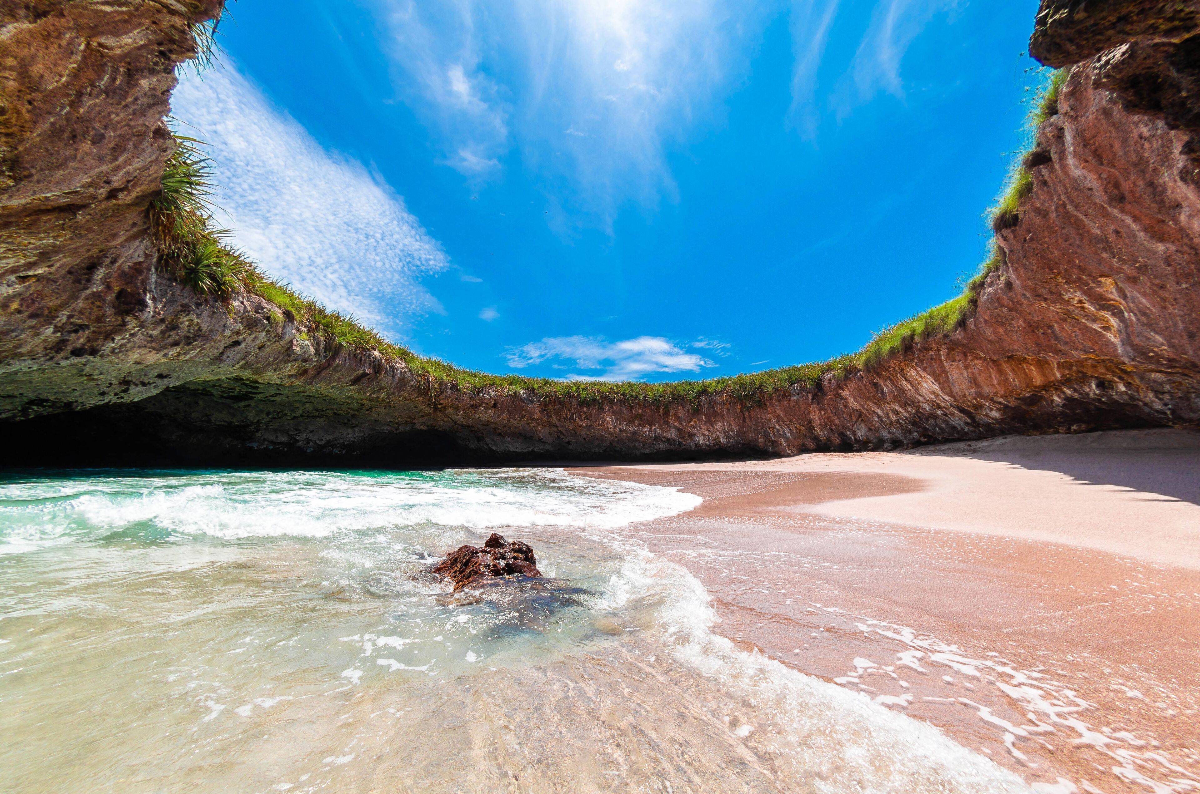 A beach with clear turquoise water, a rocky cliff, and a clear blue sky.