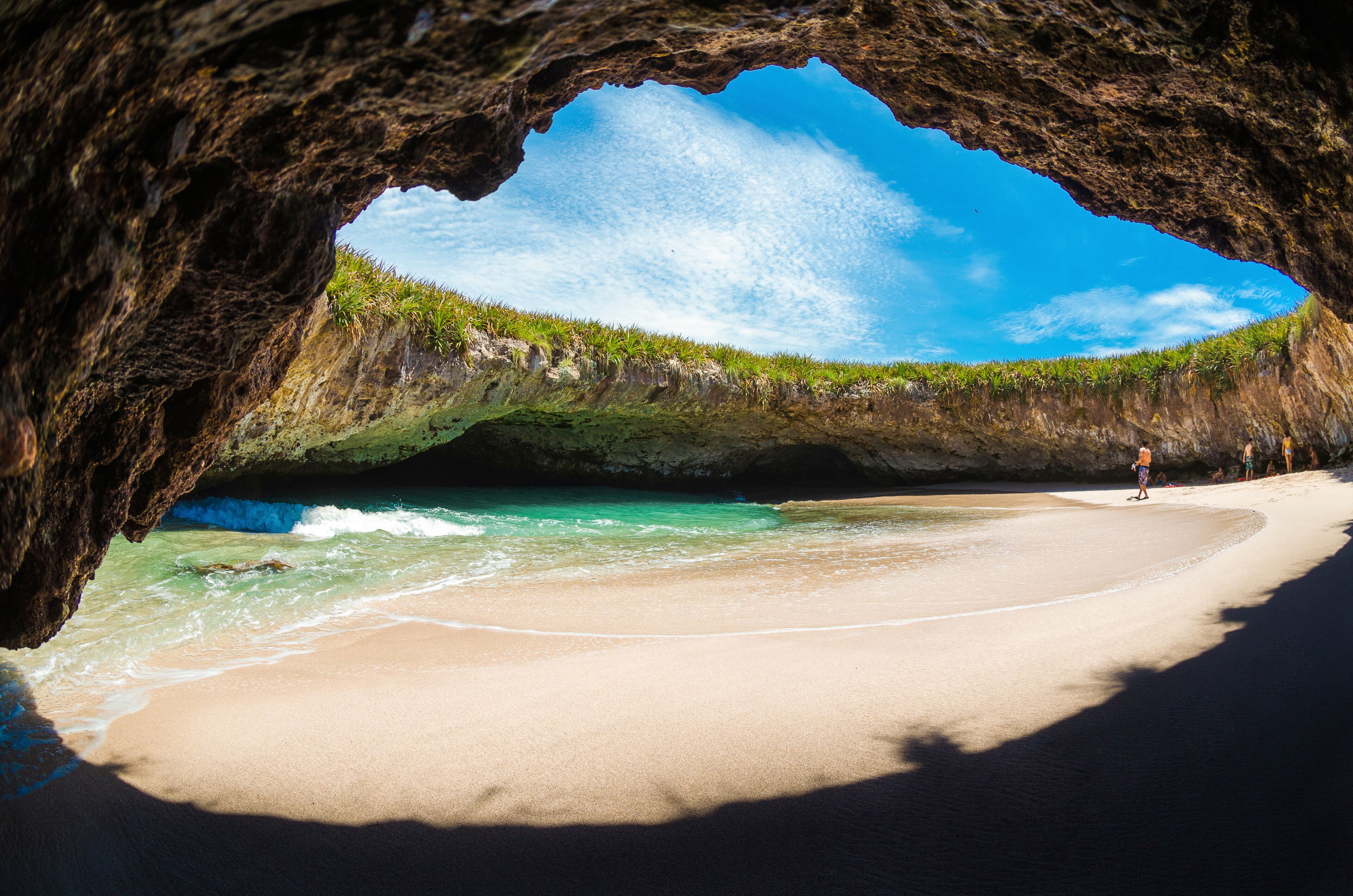 A beach with a cave entrance, clear turquoise water, and a clear blue sky.