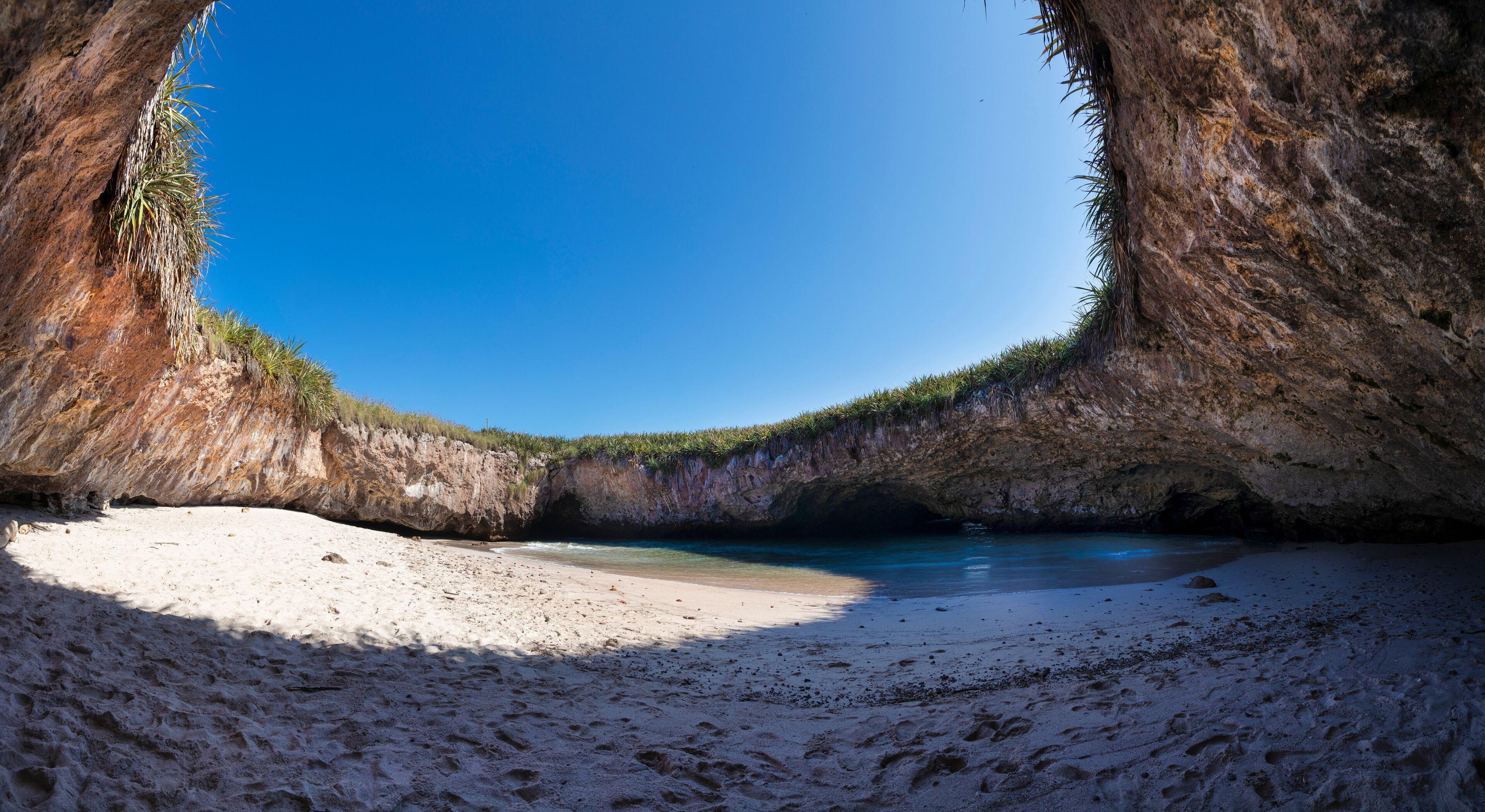 A beach with a natural rock formation arching over the water.