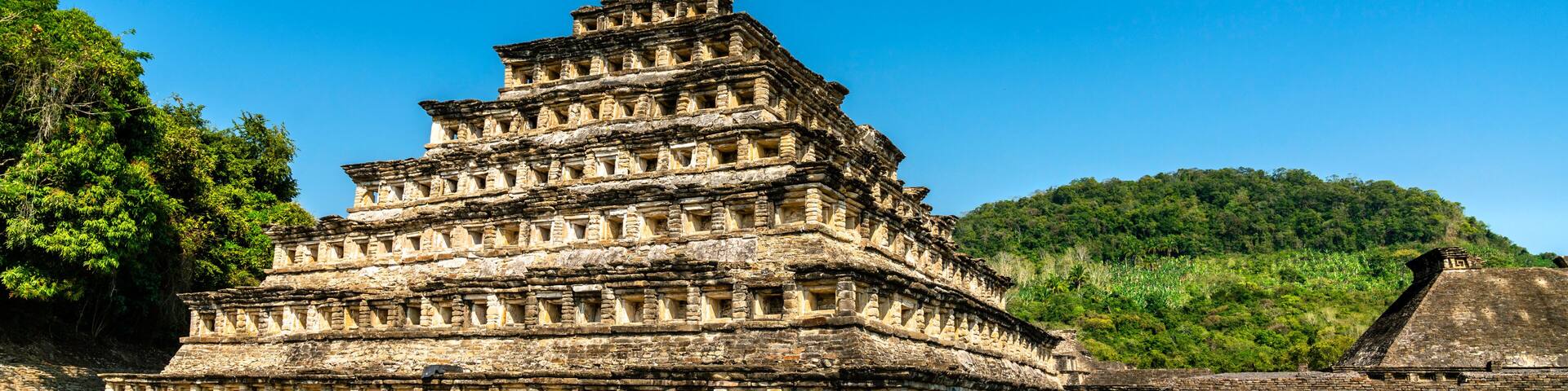 A tiered ancient pyramid structure with a surrounding stone wall and grassy area.