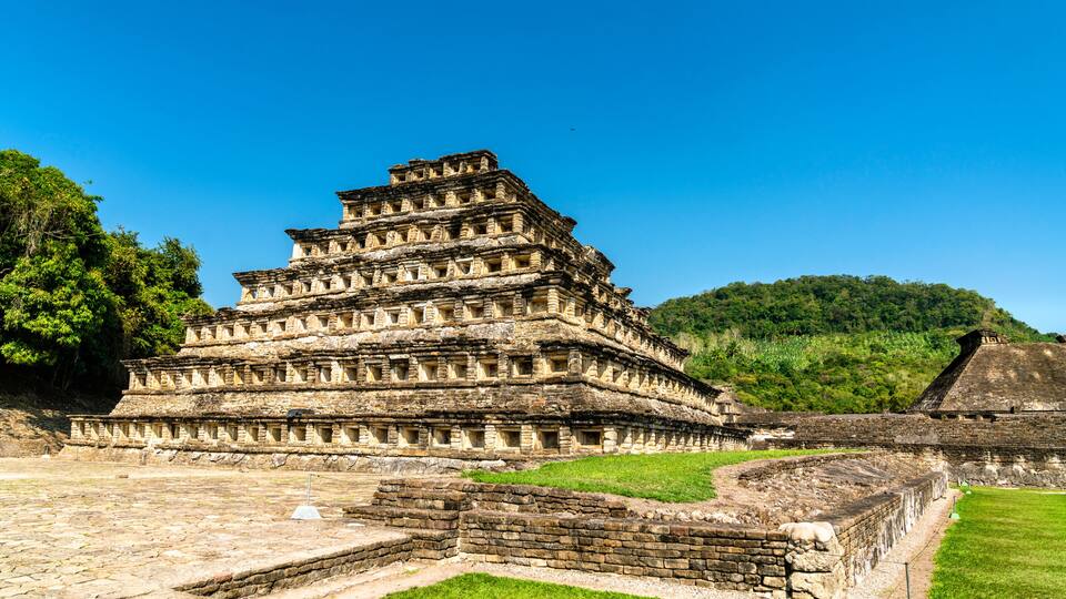 A tiered ancient pyramid structure with a surrounding stone wall and grassy area.