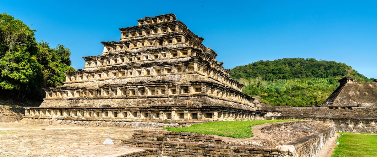 A tiered ancient pyramid structure with a surrounding stone wall and grassy area.