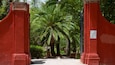 Una puerta roja con un letrero que dice "Parque Benito Juarez" que da a un camino bordeado de palmeras.