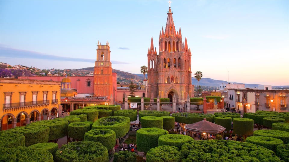A historic cathedral with a clock tower, surrounded by well-manicured gardens and other buildings.