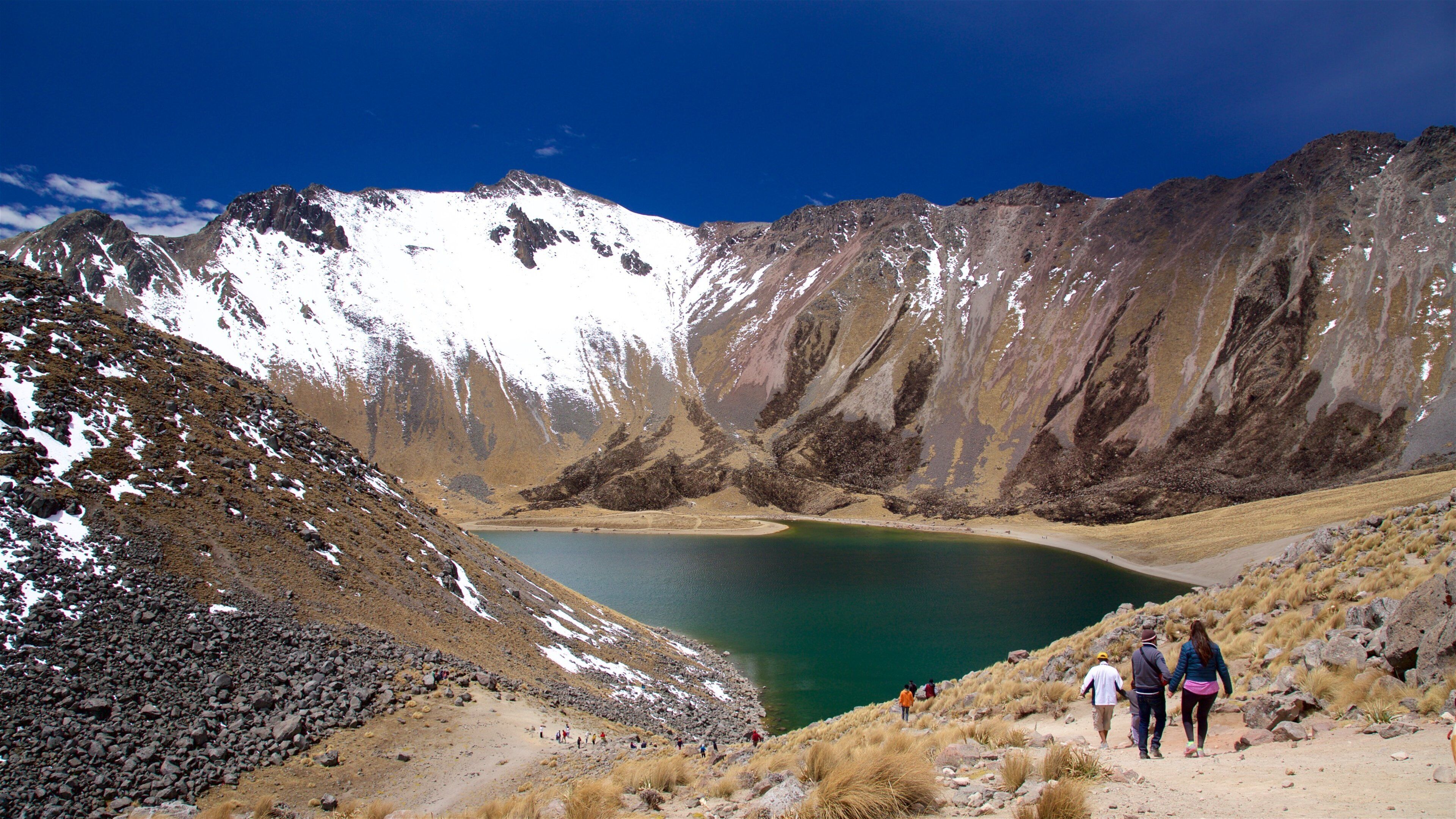 A mountainous landscape with a turquoise lake surrounded by rocky terrain and snow-capped peaks.