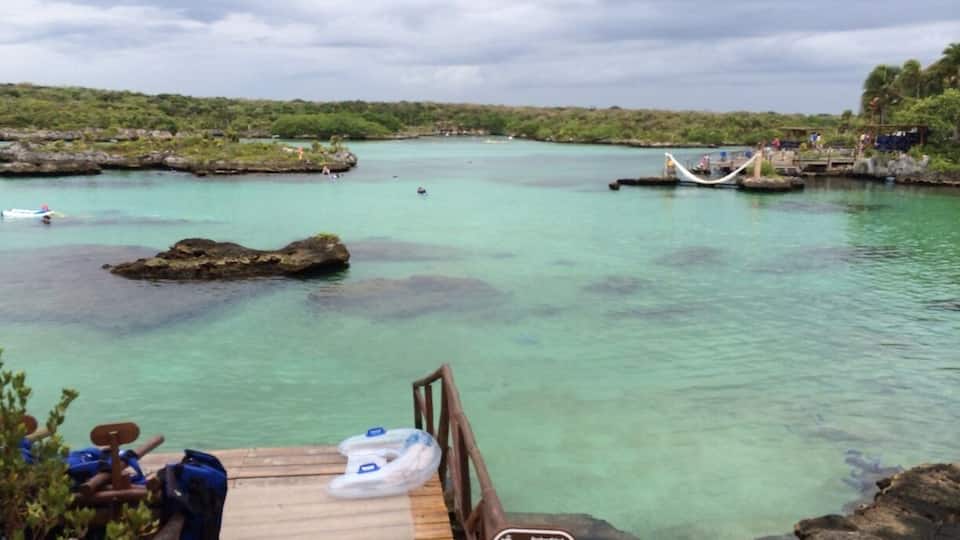 A wooden dock with clear turquoise water, a hammock, and a sign indicating a protected area.