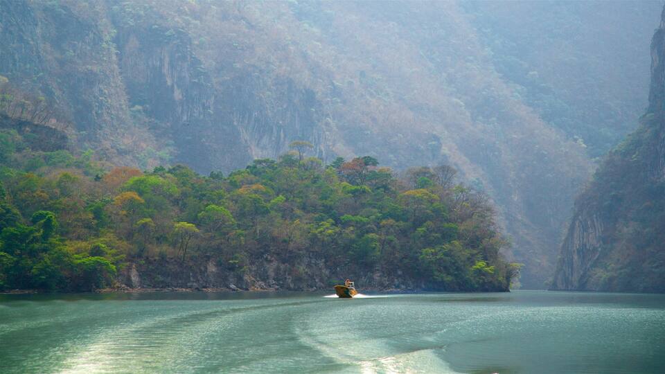 A boat on a calm river surrounded by dense green forest and steep cliffs.
