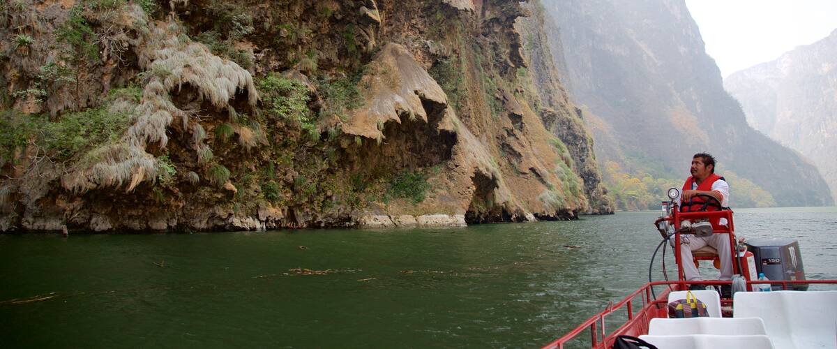 A person on a boat near a steep, rocky cliff with sparse vegetation.