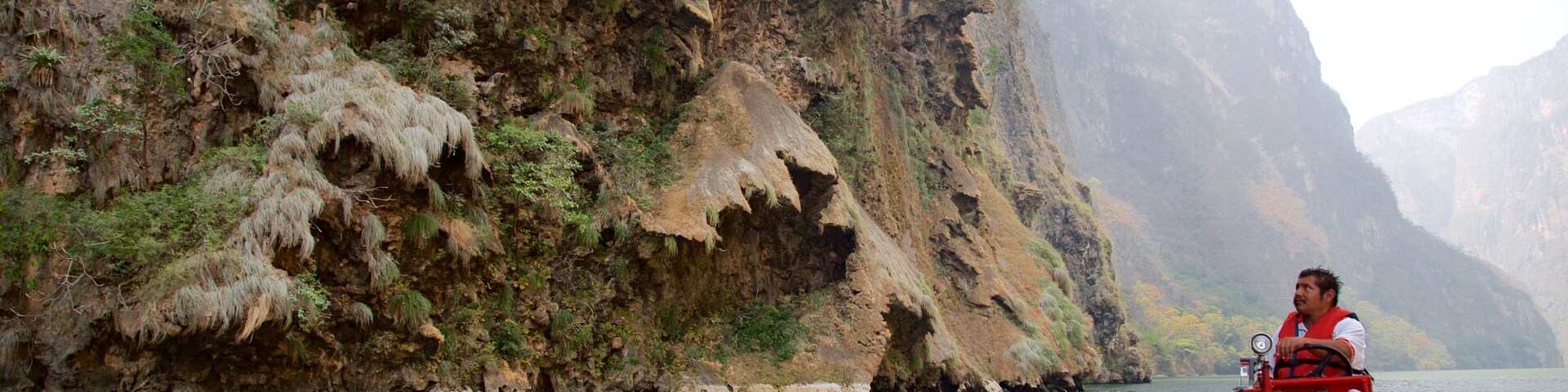 A person on a boat near a steep, rocky cliff with sparse vegetation.