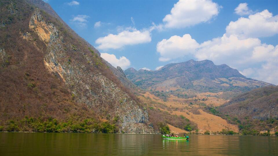 A green boat on a calm lake surrounded by rocky mountains and sparse vegetation.