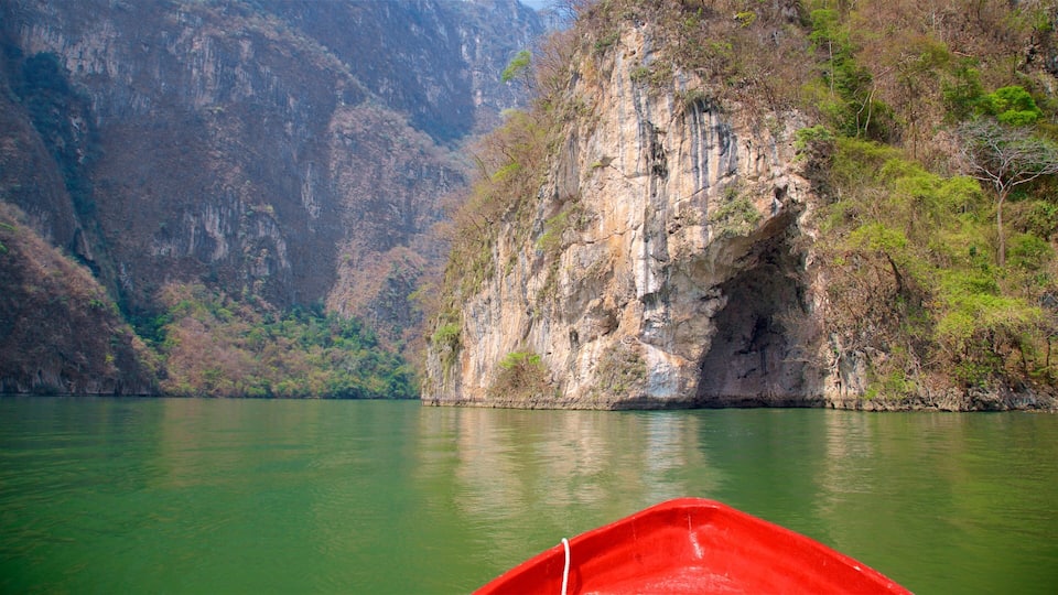 A red boat on a calm river with steep cliffs on one side.