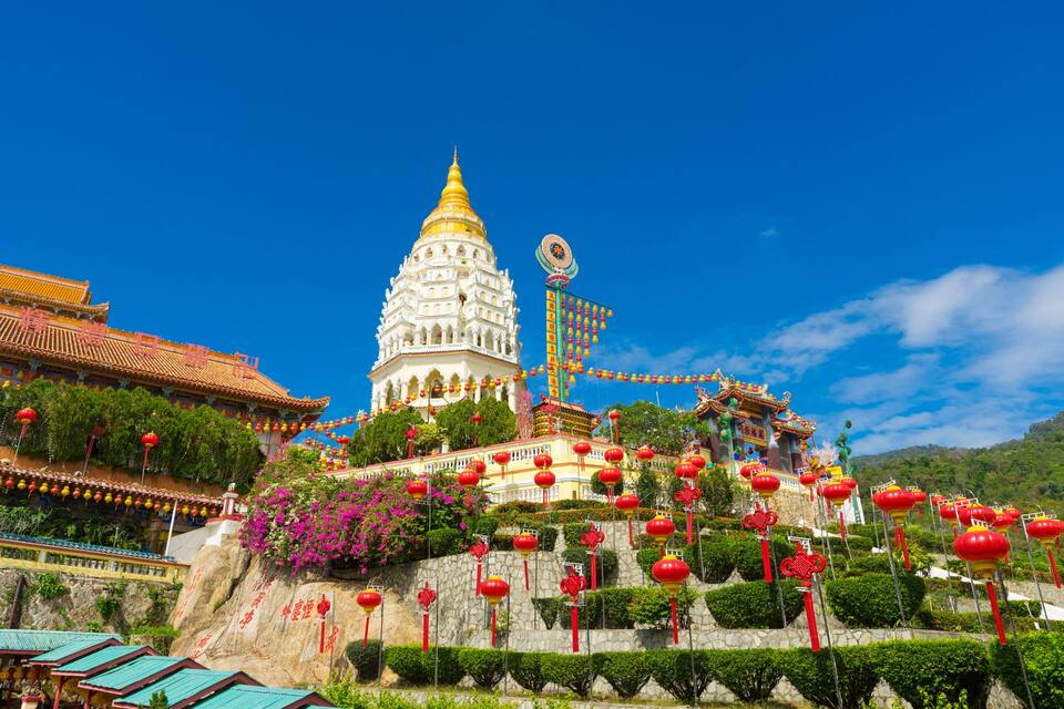 A traditional temple with a golden spire, red lanterns, and lush greenery.