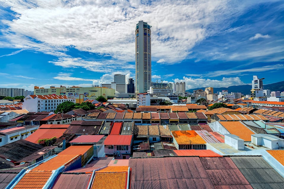 A cityscape with a prominent tall building, a variety of colorful rooftops, and a clear blue sky with scattered clouds.