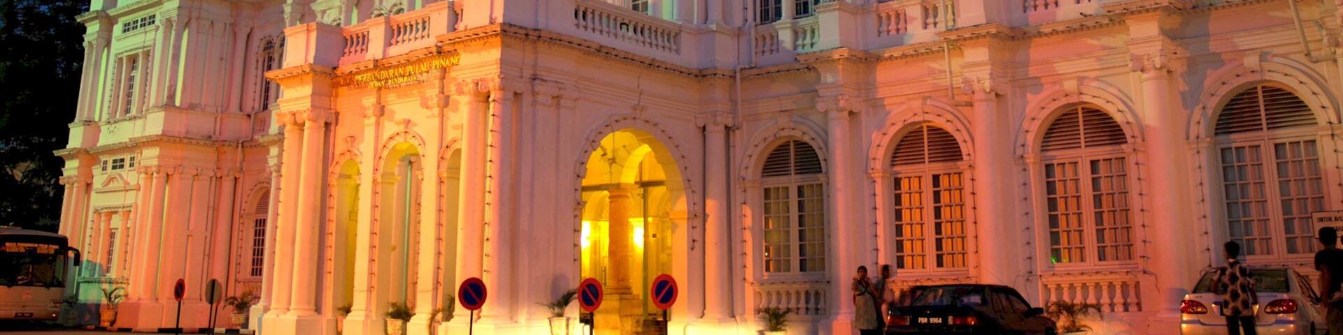 A grand, illuminated building with classical architecture, featuring multiple flags, arched windows, and a prominent entrance.