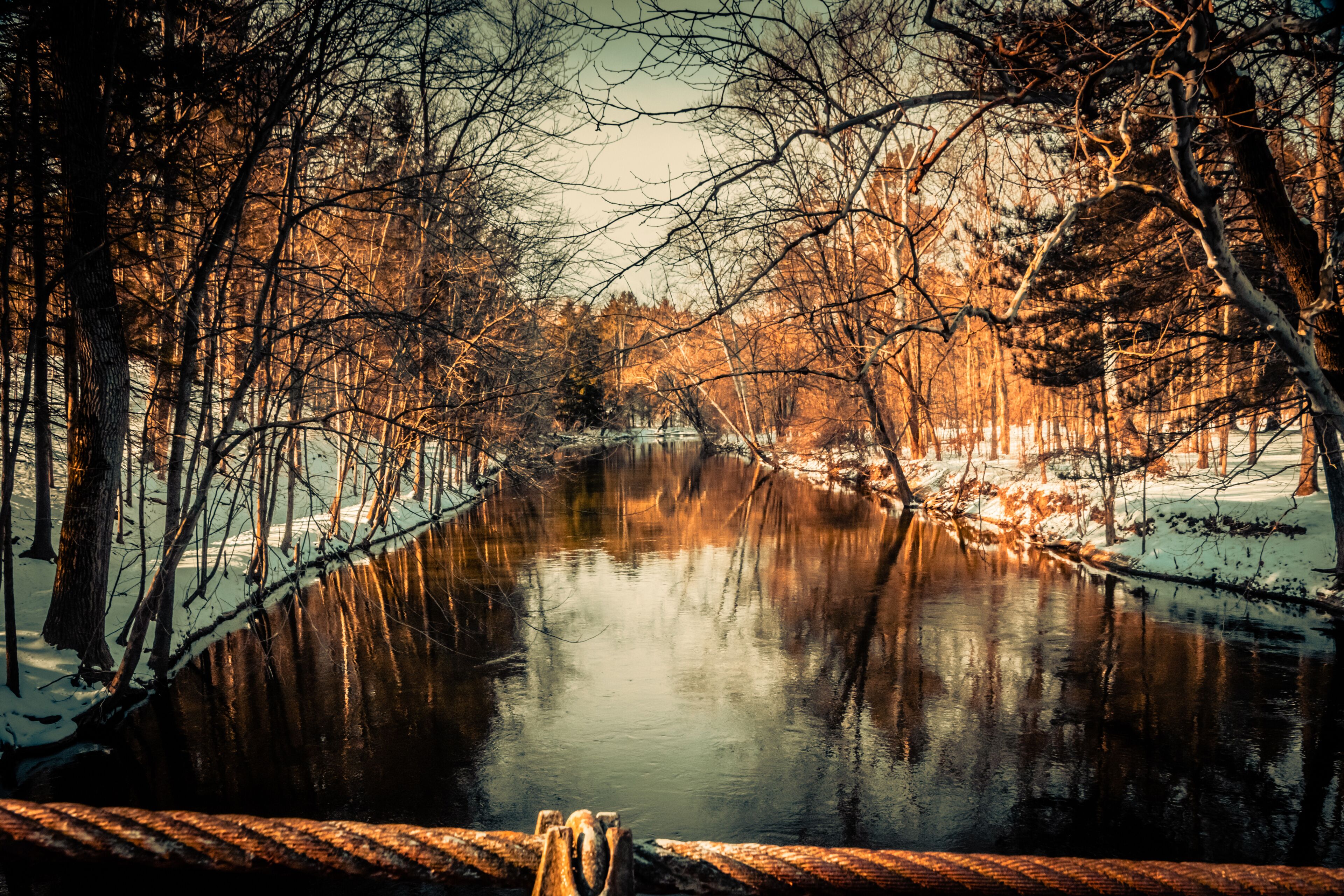 A river reflecting trees and a wooden bridge.