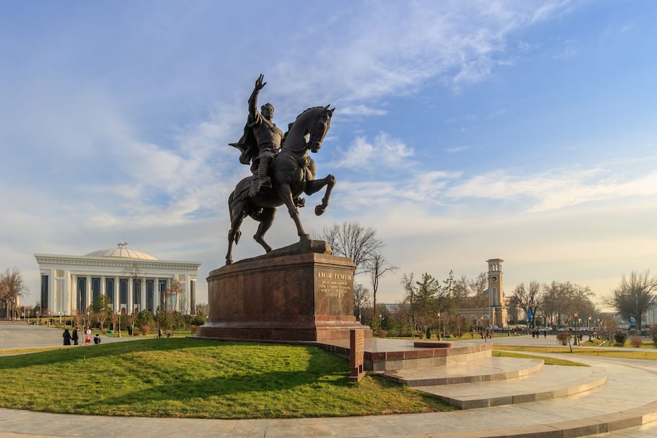 A statue of a man on horseback in a park with a building in the background.