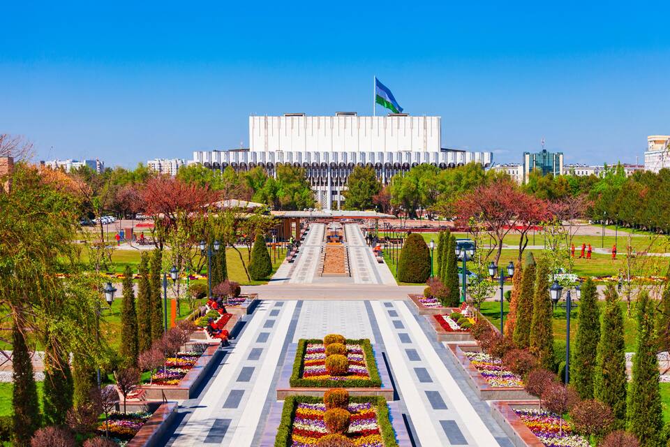 A large building with a flag, surrounded by well-maintained gardens and trees.
