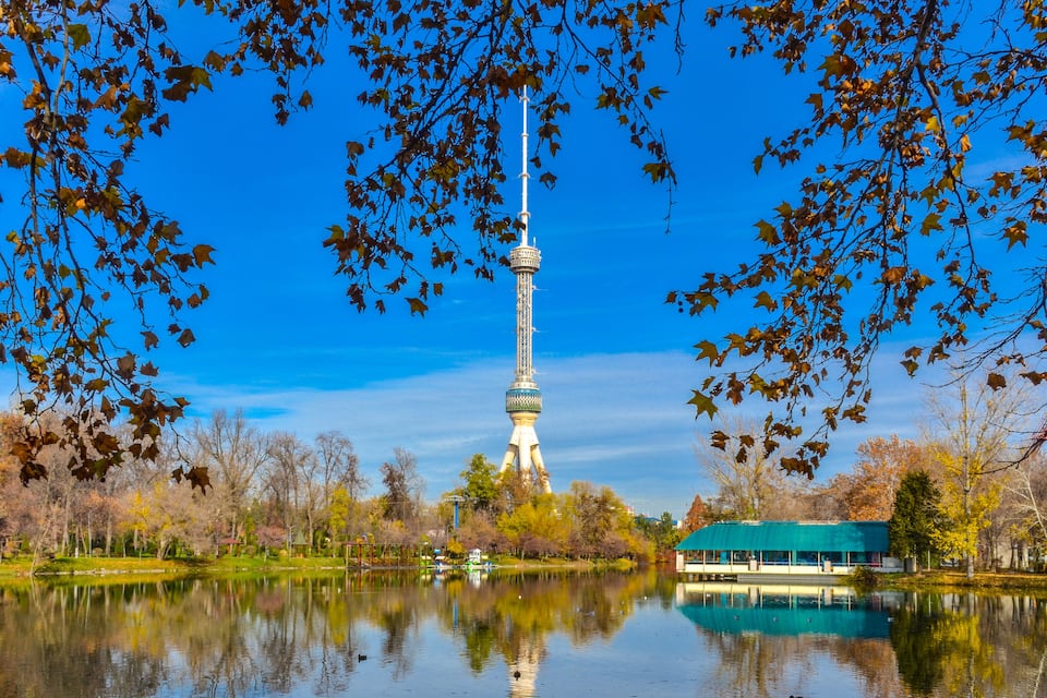 A tower reflected in a calm lake, surrounded by autumn trees and a clear blue sky.