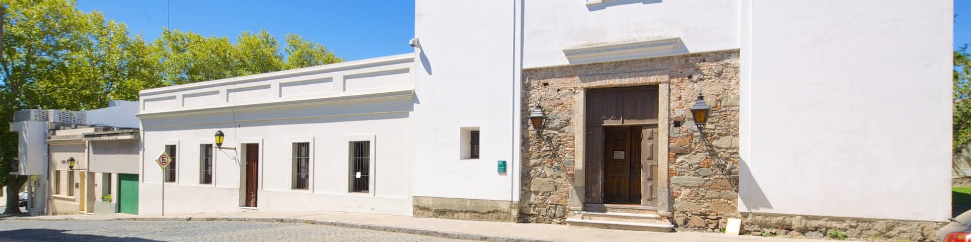 A white building with a stone entrance, a wooden door, and a window with blue-tinted glass.