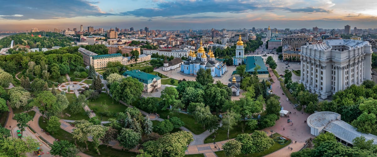 A cityscape with a river, green parks, and historic buildings with golden domes.