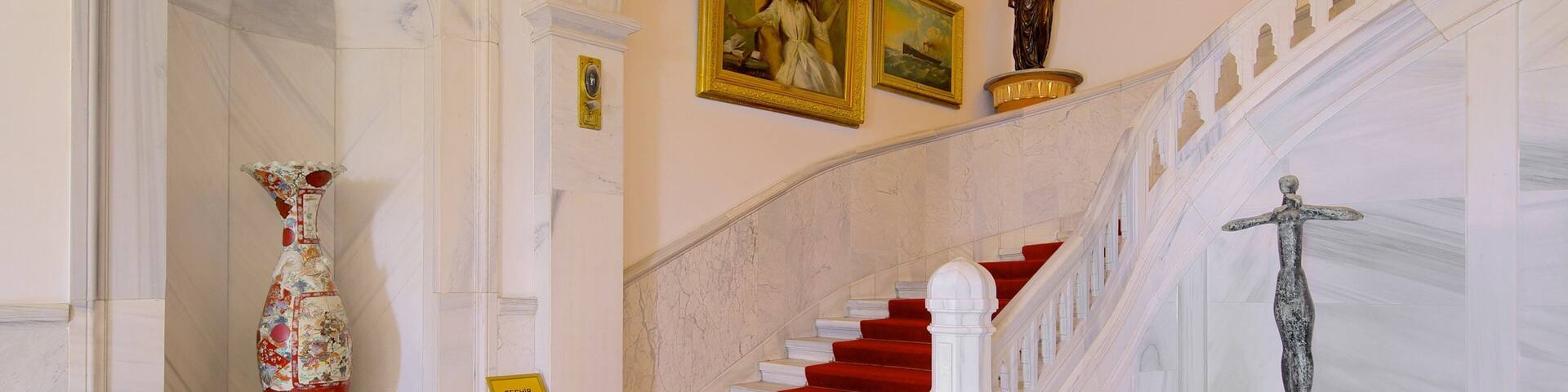 A grand staircase with red carpet, marble walls, and classical statues.