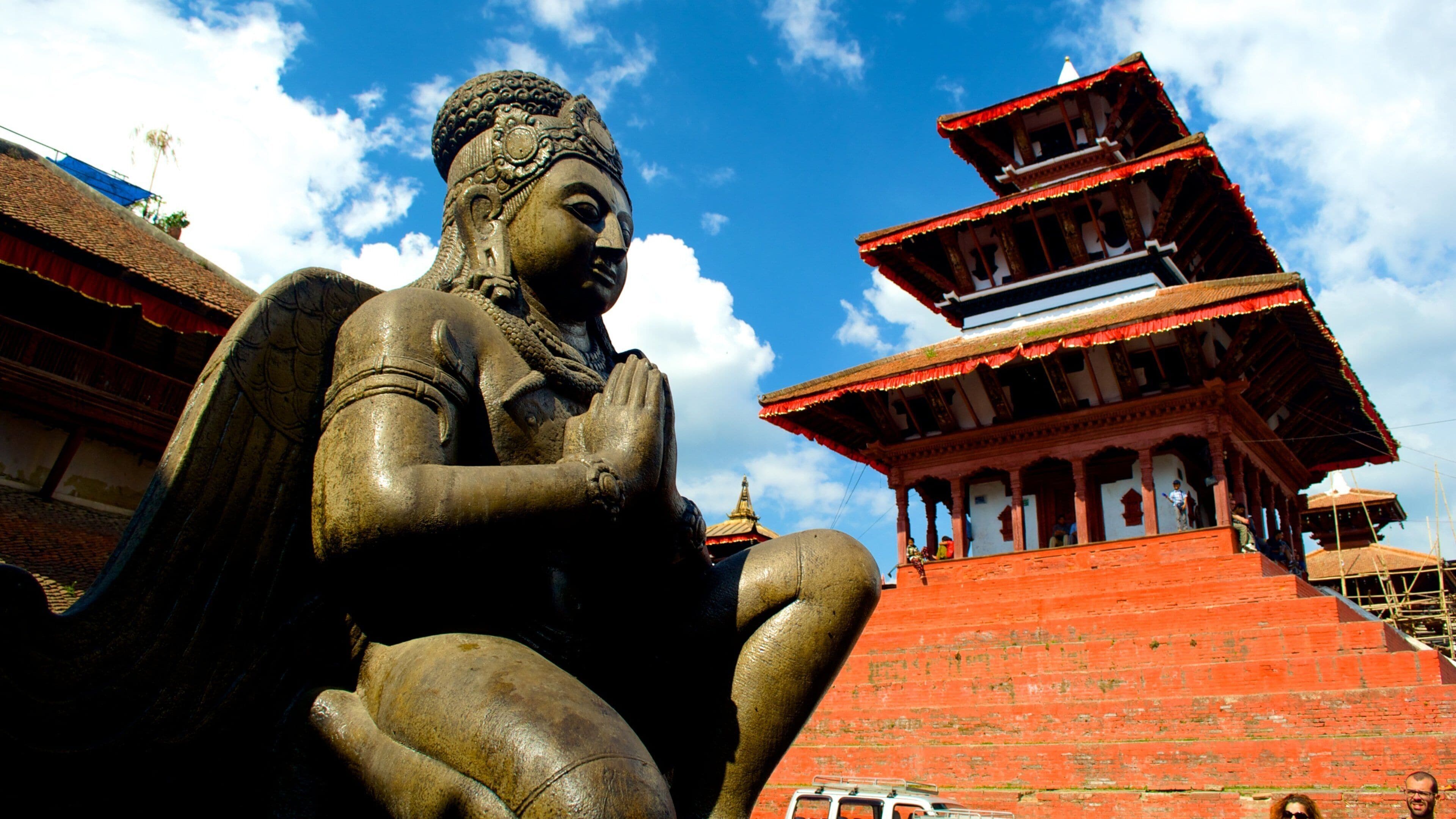 A large Buddha statue with a red-roofed temple in the background.