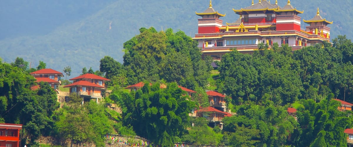 A traditional multi-tiered building with red and gold accents, surrounded by lush green trees and mountains in the background.