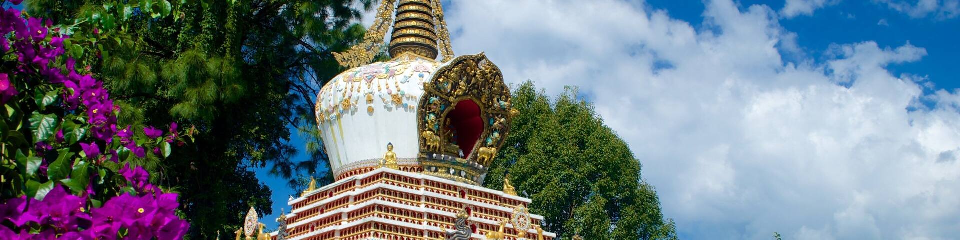 A colorful pagoda with intricate designs and a tall spire, surrounded by lush greenery and mountains.