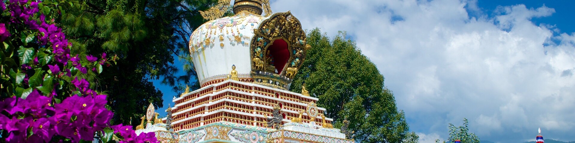 Un pagodas colorido con diseños intrincados y una aguja alta, rodeado de vegetación exuberante y montañas.