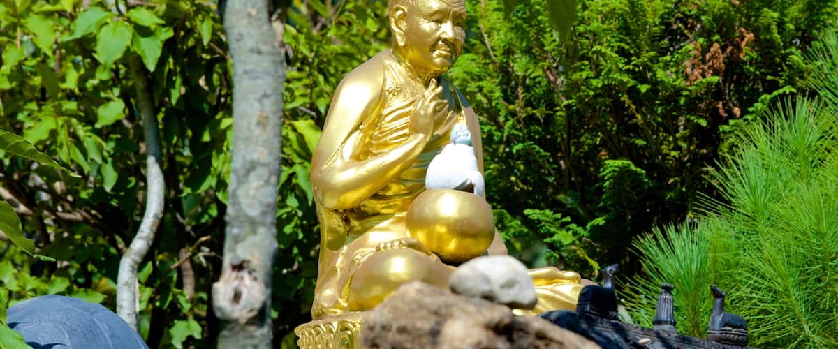 A golden Buddha statue surrounded by lush greenery and rocks.