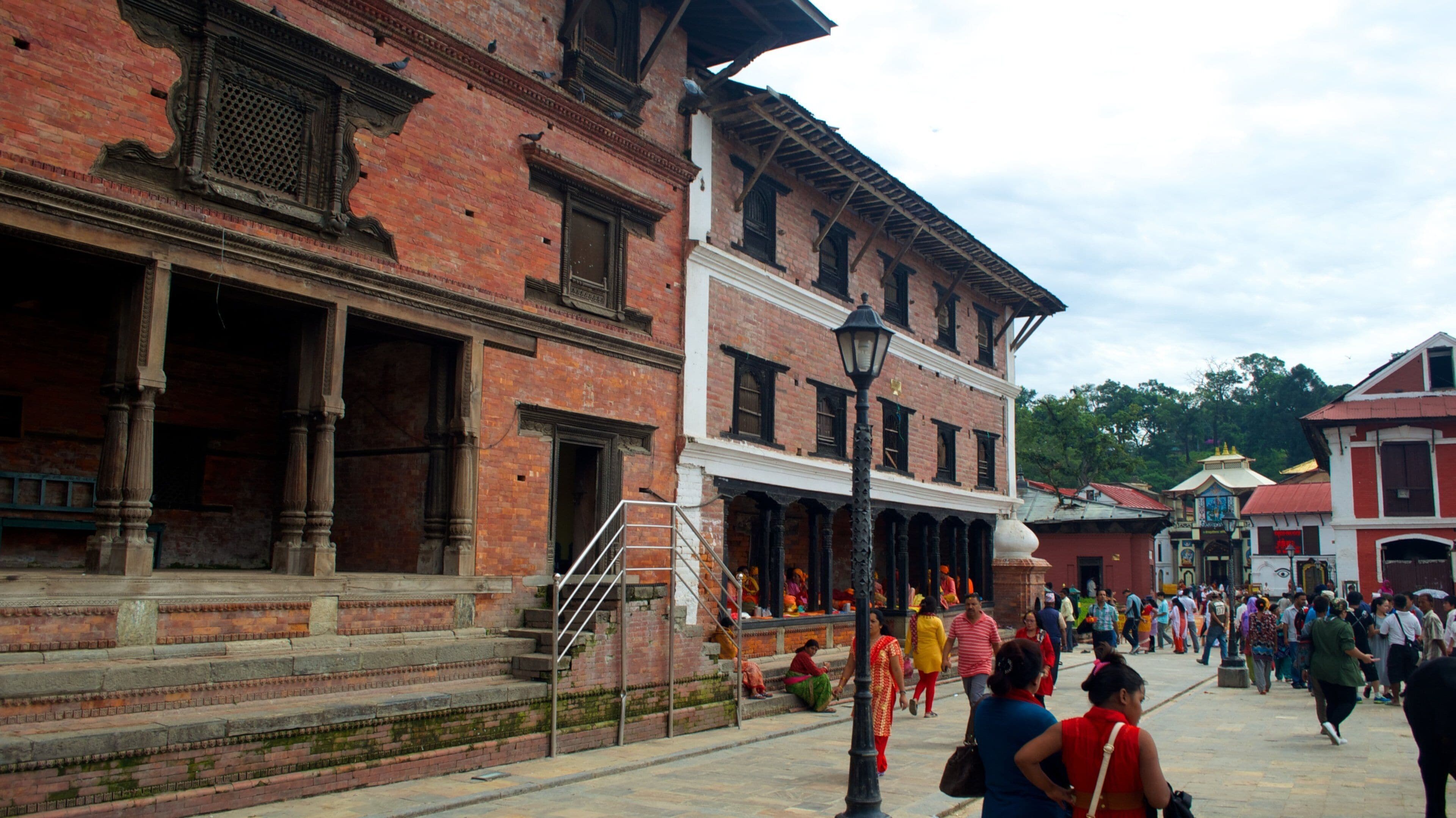 A historic building with red brick walls and white trim, featuring ornate columns and a staircase leading to an upper level.